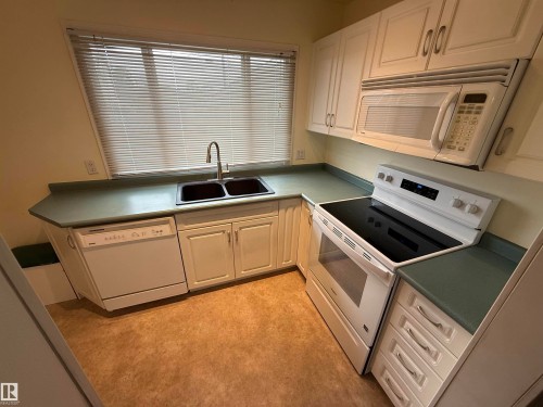 Kitchen featuring white cabinetry, a double basin sink with a gooseneck faucet, a built-in dishwasher, a smooth-top electric range, and an over-the-range microwave - 12916 95A Street, Edmonton, AB - Indoor Photo Showing Kitchen With Double Sink