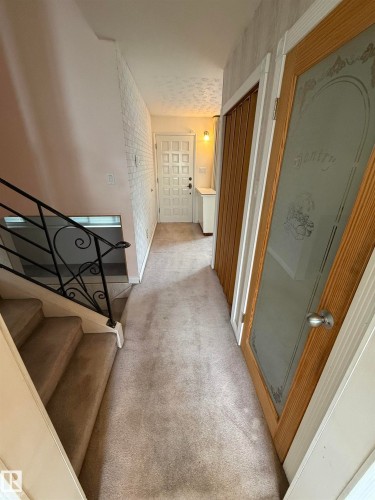 Carpeted hallway featuring a white paneled entry door, built-in shelving, and a decorative glass-paneled door - 12916 95A Street, Edmonton, AB - Indoor Photo Showing Other Room