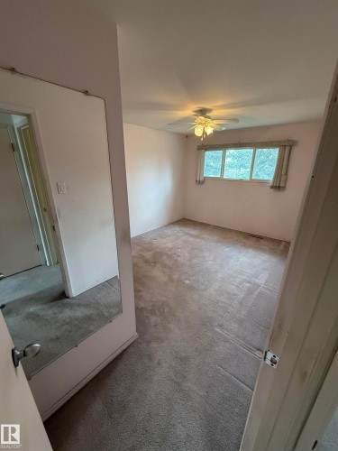 Carpeted room featuring a ceiling fan with integrated lighting, a window with horizontal blinds, and a full-length wall mirror - 12916 95A Street, Edmonton, AB - Indoor Photo Showing Other Room