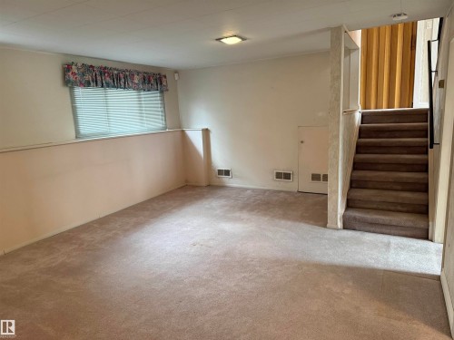 Carpeted lower level with a window, built-in storage access, and a fully carpeted staircase with a black metal handrail - 12916 95A Street, Edmonton, AB - Indoor Photo Showing Other Room