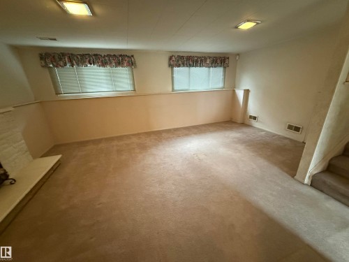 Spacious carpeted room featuring a white brick fireplace, two windows with blinds, built-in wall vents, and recessed ceiling lighting - 12916 95A Street, Edmonton, AB - Indoor Photo Showing Other Room