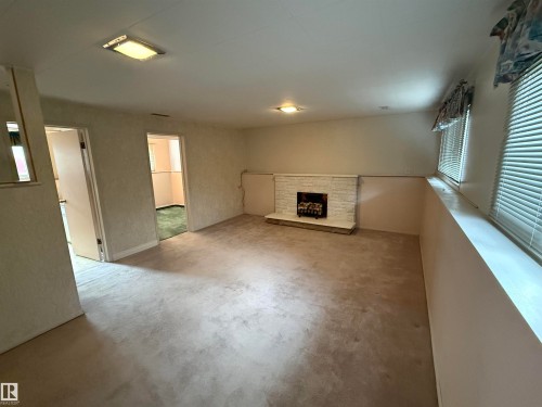 Carpeted living space featuring a white brick fireplace with a hearth, multiple windows with horizontal blinds, and overhead lighting - 12916 95A Street, Edmonton, AB - Indoor Photo Showing Other Room