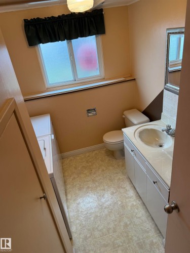 Compact bathroom featuring a white vanity with integrated sink, a toilet, a frosted window, and square-patterned vinyl flooring - 12916 95A Street, Edmonton, AB - Indoor Photo Showing Bathroom