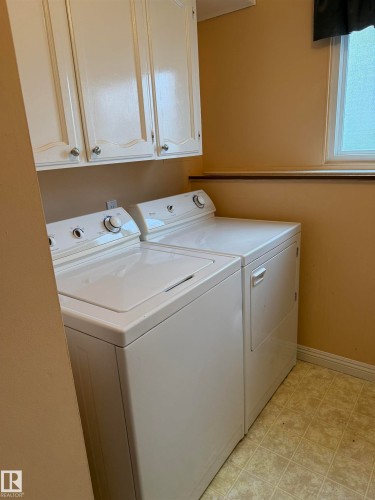 Dedicated laundry area featuring upper white cabinetry with decorative trim, a single window, and tiled flooring - 12916 95A Street, Edmonton, AB - Indoor Photo Showing Laundry Room
