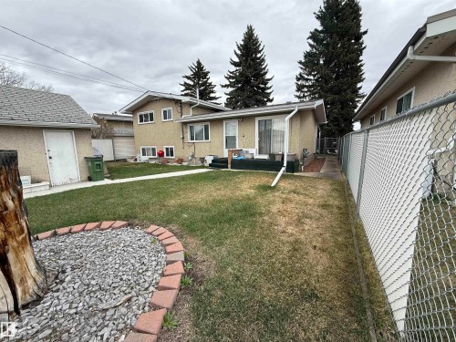 Expansive backyard featuring a central lawn area, a detached auxiliary building with a shingled roof, a rock bed with brick edging, and mature evergreen trees - 12916 95A Street, Edmonton, AB - Outdoor