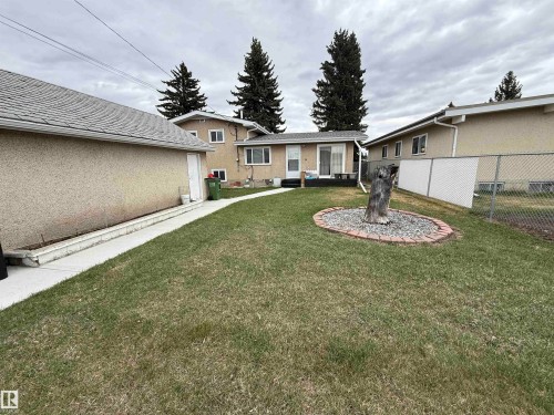 Expansive backyard featuring a concrete walkway, mature tree landscaping, chain-link fencing, and a stucco-exterior garage - 12916 95A Street, Edmonton, AB - Outdoor