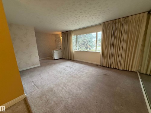 Spacious room featuring broad picture windows, textured ceiling, light-toned carpeting, and a painted brick wall detail - 12916 95A Street, Edmonton, AB - Indoor Photo Showing Other Room