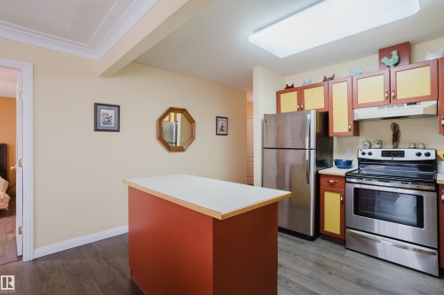 The kitchen features stainless steel appliances including a refrigerator and range, a standalone island with a light-colored countertop, and two-tone cabinetry - 25 9926 80 Avenue, Edmonton, AB - Indoor Photo Showing Kitchen