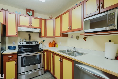 The kitchen features extensive cabinetry, a stainless steel oven with a range hood, a stainless steel microwave, and a double basin sink - 25 9926 80 Avenue, Edmonton, AB - Indoor Photo Showing Kitchen With Double Sink