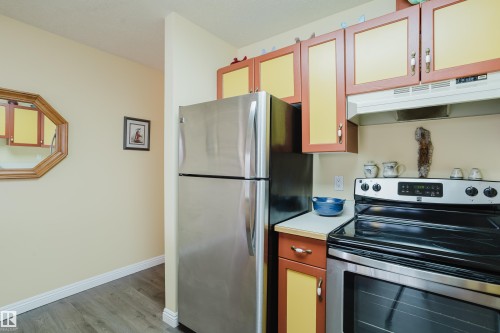The kitchen features a stainless steel refrigerator and stove, ample cabinetry, and a range hood - 25 9926 80 Avenue, Edmonton, AB - Indoor Photo Showing Kitchen