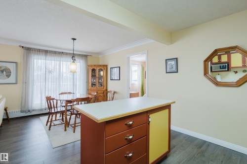 This inviting dining area features dark wood flooring, a decorative light fixture, and a large window with sheer curtains - 25 9926 80 Avenue, Edmonton, AB - Indoor