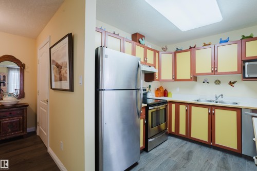The kitchen features wood-look flooring, stainless steel appliances including a refrigerator and range, a microwave, and a double basin sink - 25 9926 80 Avenue, Edmonton, AB - Indoor Photo Showing Kitchen With Double Sink