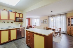The kitchen features wood cabinetry with contrasting paneling, stainless steel appliances, and a central island with countertop space - 