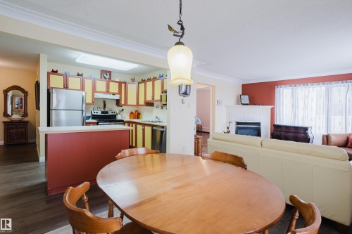 The property features a kitchen with yellow and red cabinetry, stainless steel refrigerator, and a dishwasher - 25 9926 80 Avenue, Edmonton, AB - Indoor Photo Showing Dining Room With Fireplace