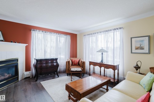 Living area featuring dark flooring, a white mantel with a fireplace, and windows with sheer white curtains - 25 9926 80 Avenue, Edmonton, AB - Indoor Photo Showing Living Room With Fireplace