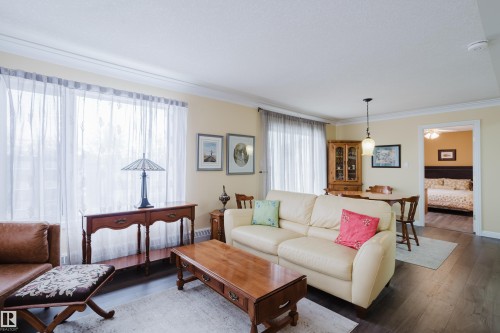 The living area features warm-toned walls, dark wood flooring, and crown molding - 25 9926 80 Avenue, Edmonton, AB - Indoor Photo Showing Living Room