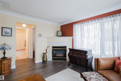 Living room with dark wood flooring, a fireplace with a white tile surround, and a large window - 25 9926 80 Avenue, Edmonton, AB - Indoor Photo Showing Living Room With Fireplace