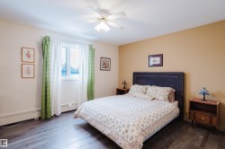 This bedroom features dark wood-style flooring, a window with curtains, and a ceiling fan - 