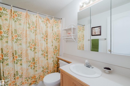 This bathroom features a vanity with an integrated sink, a large mirror, and a toilet - 25 9926 80 Avenue, Edmonton, AB - Indoor Photo Showing Bathroom