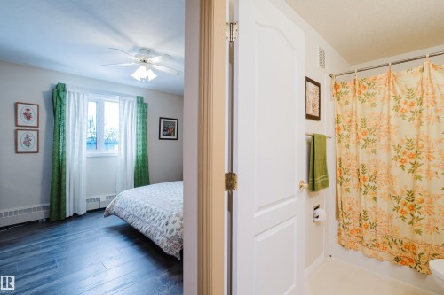 This property features a bedroom with hardwood-style flooring and a ceiling fan, complemented by a window with white and green drapes - 25 9926 80 Avenue, Edmonton, AB - Indoor Photo Showing Other Room