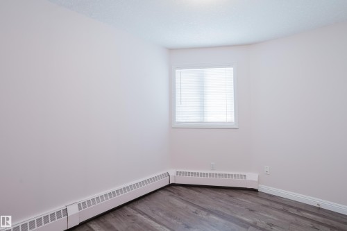 The property features neutral-toned walls, wood flooring, and a window with blinds - 25 9926 80 Avenue, Edmonton, AB - Indoor Photo Showing Other Room