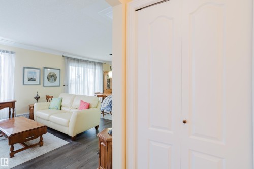 Living area with light-colored walls and dark flooring, featuring a light-colored sofa and windows with sheer curtains - 25 9926 80 Avenue, Edmonton, AB - Indoor Photo Showing Living Room