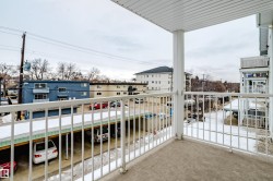 The property features a private balcony with a concrete floor and a white metal railing, providing a view of the surrounding neighborhood and covered parking spaces - 