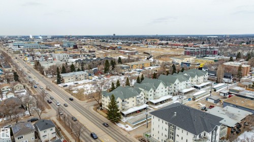 Aerial view of the neighborhood featuring a wide road, residential buildings with pitched roofs, and commercial structures in the distance - 25 9926 80 Avenue, Edmonton, AB - Outdoor With View