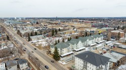 Aerial view of the neighborhood featuring a wide road, residential buildings with pitched roofs, and commercial structures in the distance - 