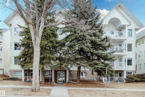 The property features a multi-story building with balconies, a pitched roof, and mature evergreen trees - 25 9926 80 Avenue, Edmonton, AB - Outdoor With Balcony With Facade