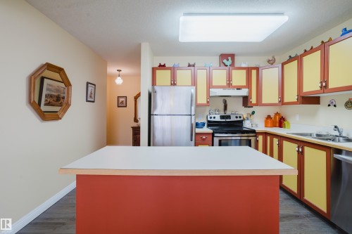 The kitchen features an island with a white countertop, a stainless steel refrigerator, a stainless steel range with an overhead microwave, and a stainless steel dishwasher - 25 9926 80 Avenue, Edmonton, AB - Indoor Photo Showing Kitchen With Double Sink