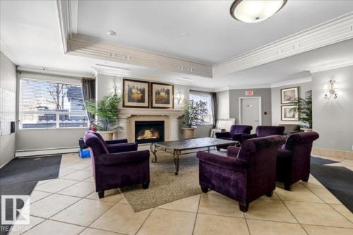 Lobby featuring a fireplace with a stone surround, crown molding, large picture windows, tile flooring, and wall sconces - 701 9707 105 Street, Edmonton, AB - Indoor With Fireplace