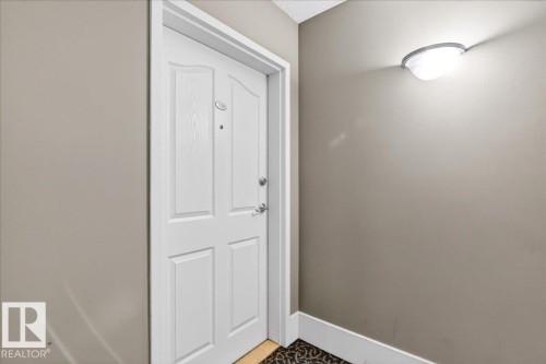 Entry door with panel detailing, coordinating trim, and a modern wall-mounted light fixture - 701 9707 105 Street, Edmonton, AB - Indoor Photo Showing Other Room