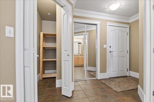 Tiled entry foyer featuring a white paneled door, crown molding, baseboards, and a flush mount ceiling light - 701 9707 105 Street, Edmonton, AB - Indoor Photo Showing Other Room