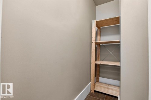 Built-in wood shelving unit featuring four tiers, neutral wall paint, white baseboards, and tile flooring - 701 9707 105 Street, Edmonton, AB - Indoor