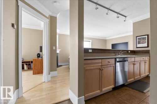 Kitchen featuring wood-finish cabinetry, stainless steel dishwasher, and track lighting - 701 9707 105 Street, Edmonton, AB - Indoor