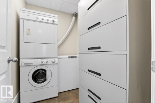 Dedicated laundry area featuring a stacked washer and dryer, a freestanding freezer, and a white storage cabinet with integrated black pulls - 701 9707 105 Street, Edmonton, AB - Indoor Photo Showing Laundry Room