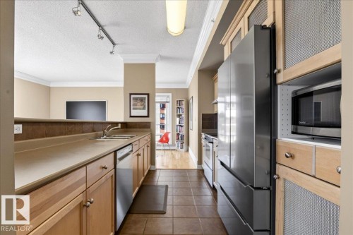 Kitchen featuring wood-finish cabinetry, stainless steel appliances, tiled flooring, and a breakfast bar - 701 9707 105 Street, Edmonton, AB - Indoor Photo Showing Kitchen With Double Sink