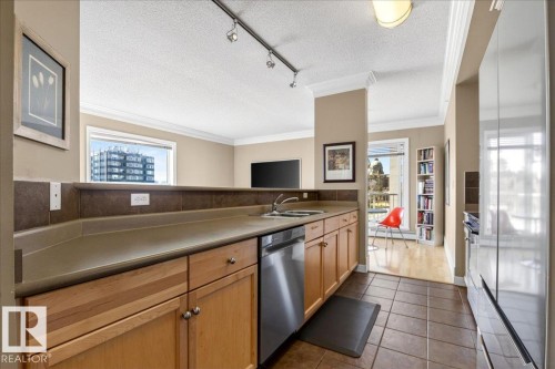 Kitchen featuring light wood cabinetry, stainless steel dishwasher, and a stone-finish countertop with an integrated sink - 701 9707 105 Street, Edmonton, AB - Indoor Photo Showing Kitchen With Double Sink