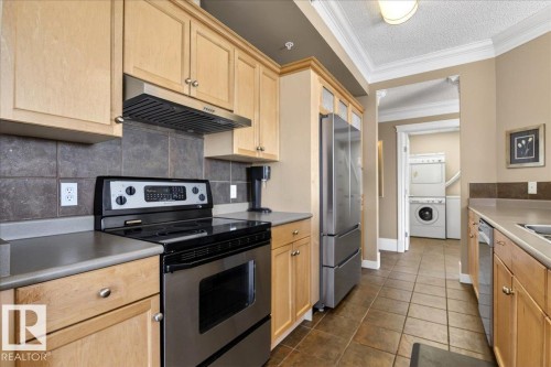 Kitchen featuring light wood cabinetry, stone-finish countertops, stainless steel appliances, and a tiled backsplash - 701 9707 105 Street, Edmonton, AB - Indoor Photo Showing Kitchen
