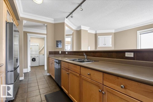 Kitchen featuring wood cabinetry, stainless steel refrigerator, integrated dishwasher, and a double basin sink - 701 9707 105 Street, Edmonton, AB - Indoor Photo Showing Kitchen With Double Sink