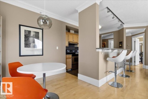 Open-concept living space with blonde wood-finish flooring, a breakfast bar, and crown molding - 701 9707 105 Street, Edmonton, AB - Indoor
