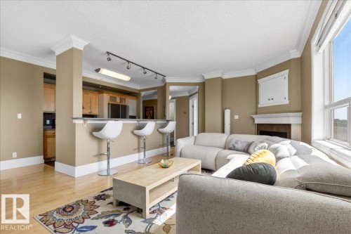 Bright living area featuring a fireplace with a white mantel, crown molding, and wood-finish flooring - 701 9707 105 Street, Edmonton, AB - Indoor Photo Showing Living Room With Fireplace