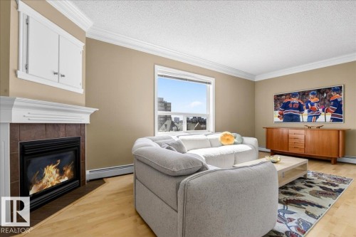 Living room featuring a fireplace with a tiled surround, a white mantel, and built-in cabinetry above - 701 9707 105 Street, Edmonton, AB - Indoor Photo Showing Living Room With Fireplace