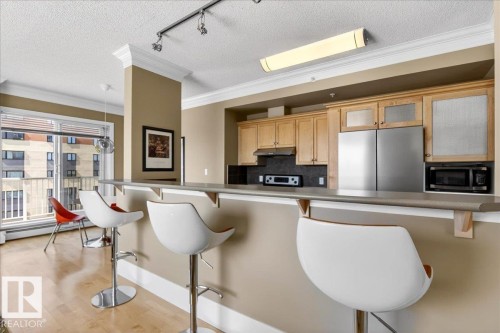 Open-concept kitchen with wood-finish cabinetry, stainless steel appliances, and a breakfast bar - 701 9707 105 Street, Edmonton, AB - Indoor Photo Showing Kitchen