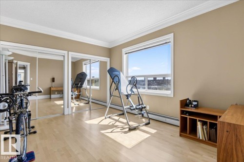 Wide window offering expansive outdoor views, light wood-finish flooring, two sets of mirrored sliding closet doors, crown molding, and neutral wall tones - 701 9707 105 Street, Edmonton, AB - Indoor Photo Showing Gym Room