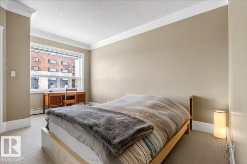 Windowed bedroom featuring neutral wall tones, white crown molding, textured carpet flooring, and a baseboard heating unit - 701 9707 105 Street, Edmonton, AB - Indoor Photo Showing Bedroom