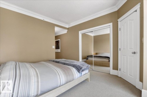 Carpeted room featuring crown molding, a white paneled door, and a mirrored closet with sliding doors - 701 9707 105 Street, Edmonton, AB - Indoor Photo Showing Bedroom