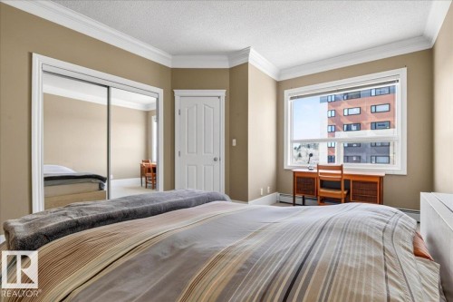 Bedroom featuring a large window, mirrored sliding closet doors, crown molding, baseboards, and a white interior door - 701 9707 105 Street, Edmonton, AB - Indoor Photo Showing Bedroom