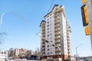 Multi-story residential building featuring a light-colored facade, individual balconies with white railings, and a contrasting dark roofline - 701 9707 105 Street, Edmonton, AB  - Outdoor With Balcony With Facade 